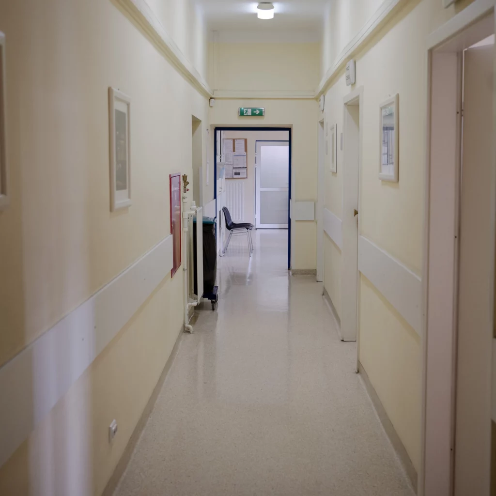 Korytarz w przychodni z drzwiami do gabinetów i krzesłami na końcu korytarza