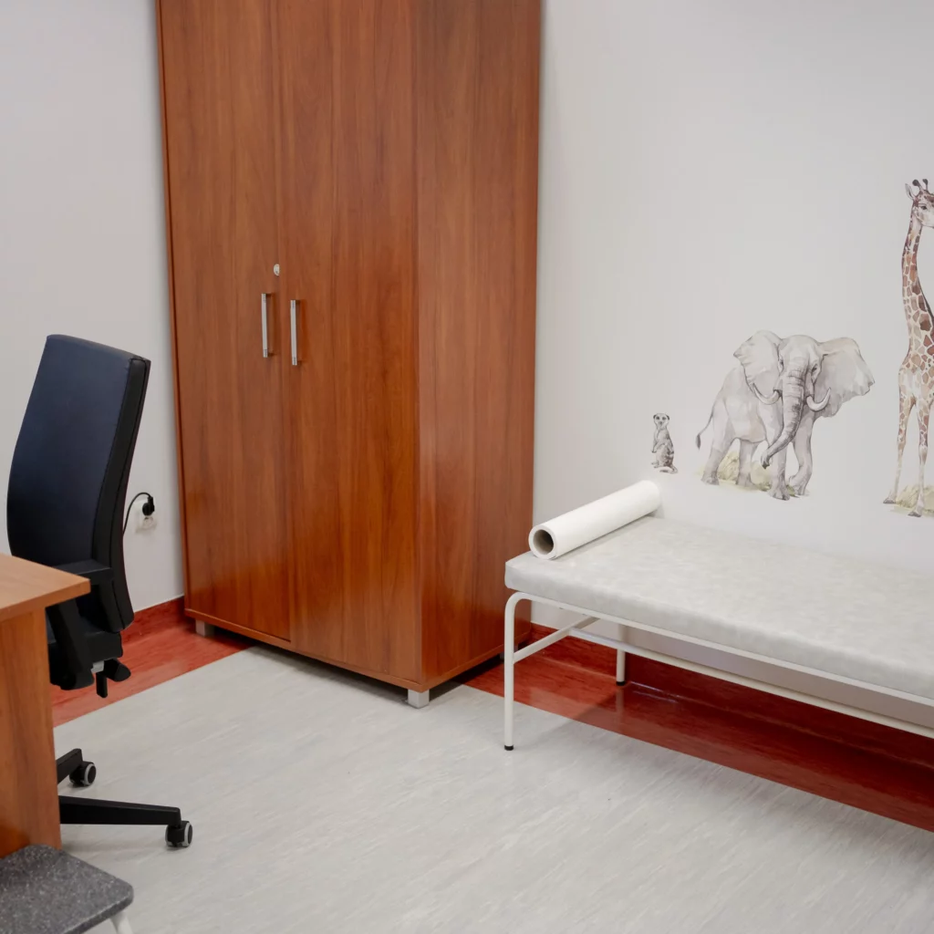 Gabinet lekarski z kozetką, krzesłem i szafą, ozdobiony naklejkami zwierząt na ścianie