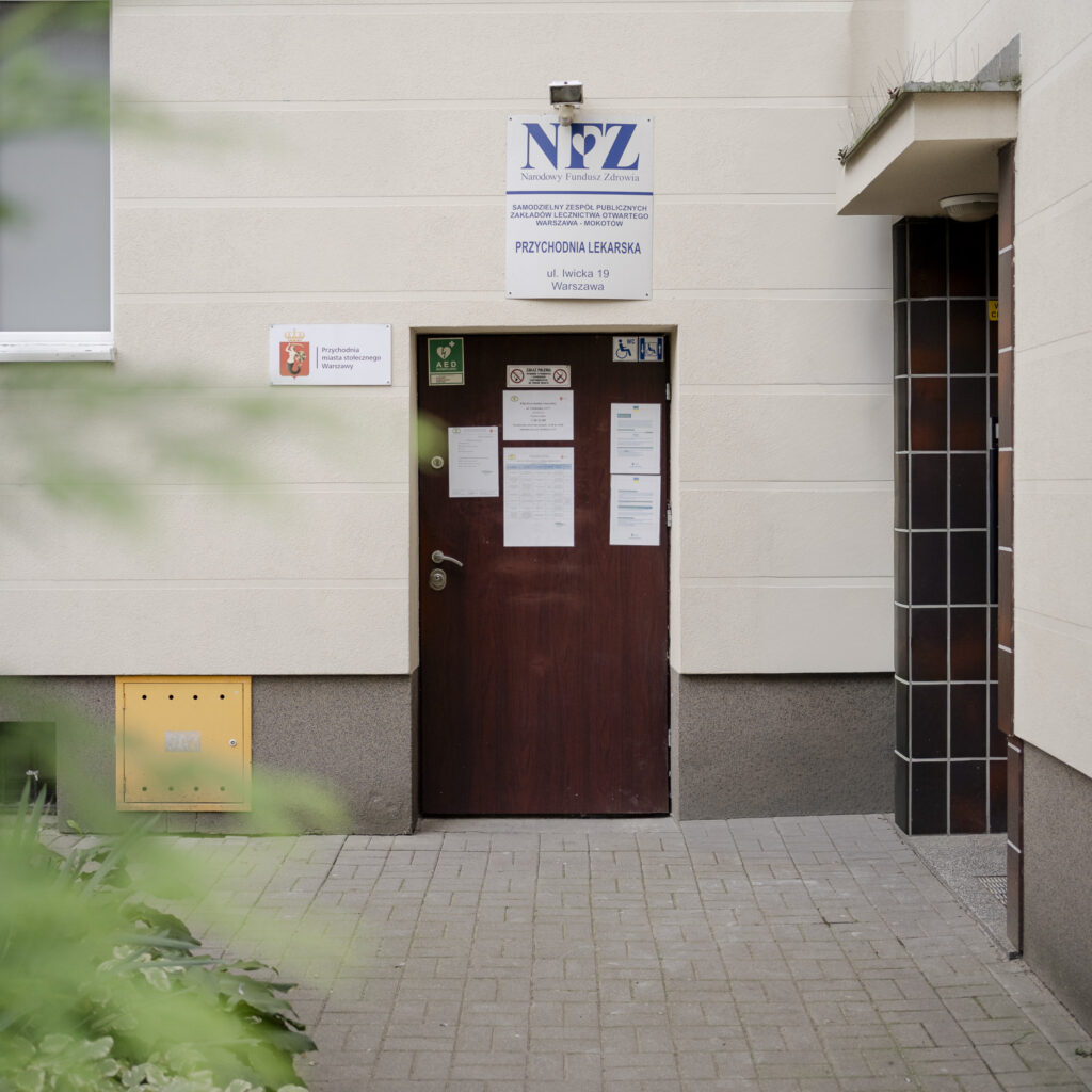 Wejście do przychodni lekarskiej z tablicą NFZ i herbem Warszawy