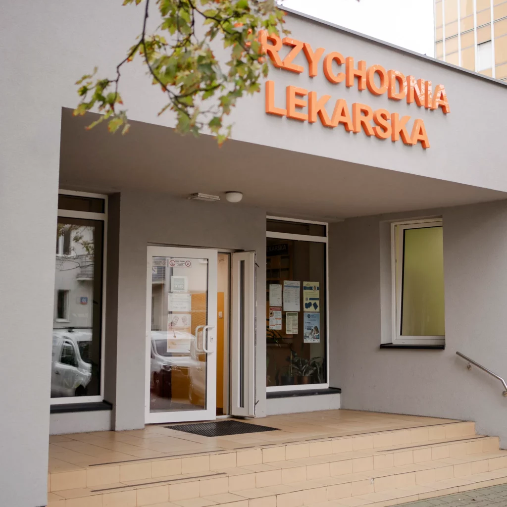 Wejście do przychodni lekarskiej z pomarańczowym napisem nad drzwiami