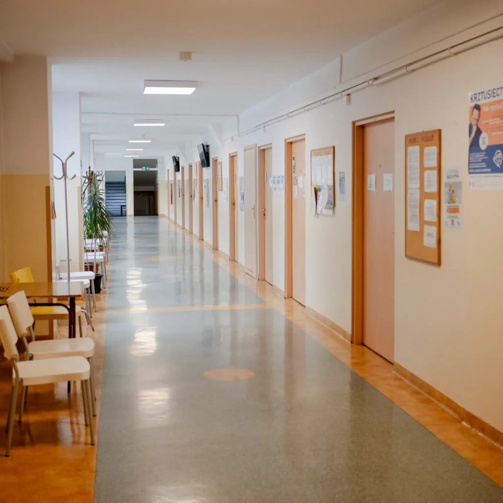 Korytarz przychodni z drzwiami do gabinetów lekarskich i tablicami informacyjnymi na ścianach