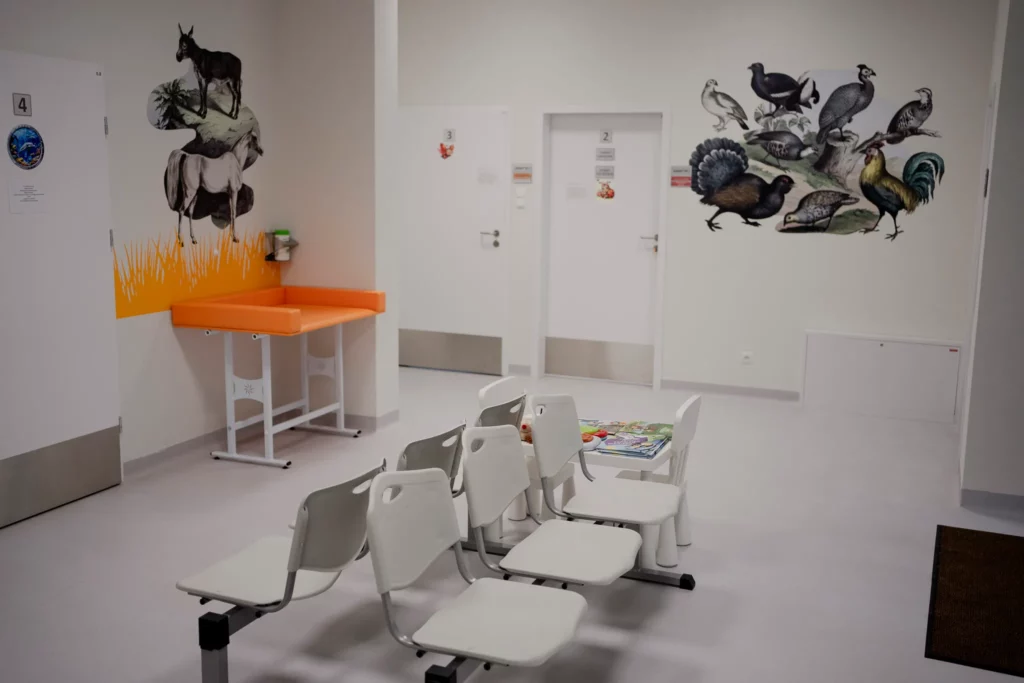 Poczekalnia w przychodni z białymi krzesłami i kolorowymi ilustracjami zwierząt na ścianach