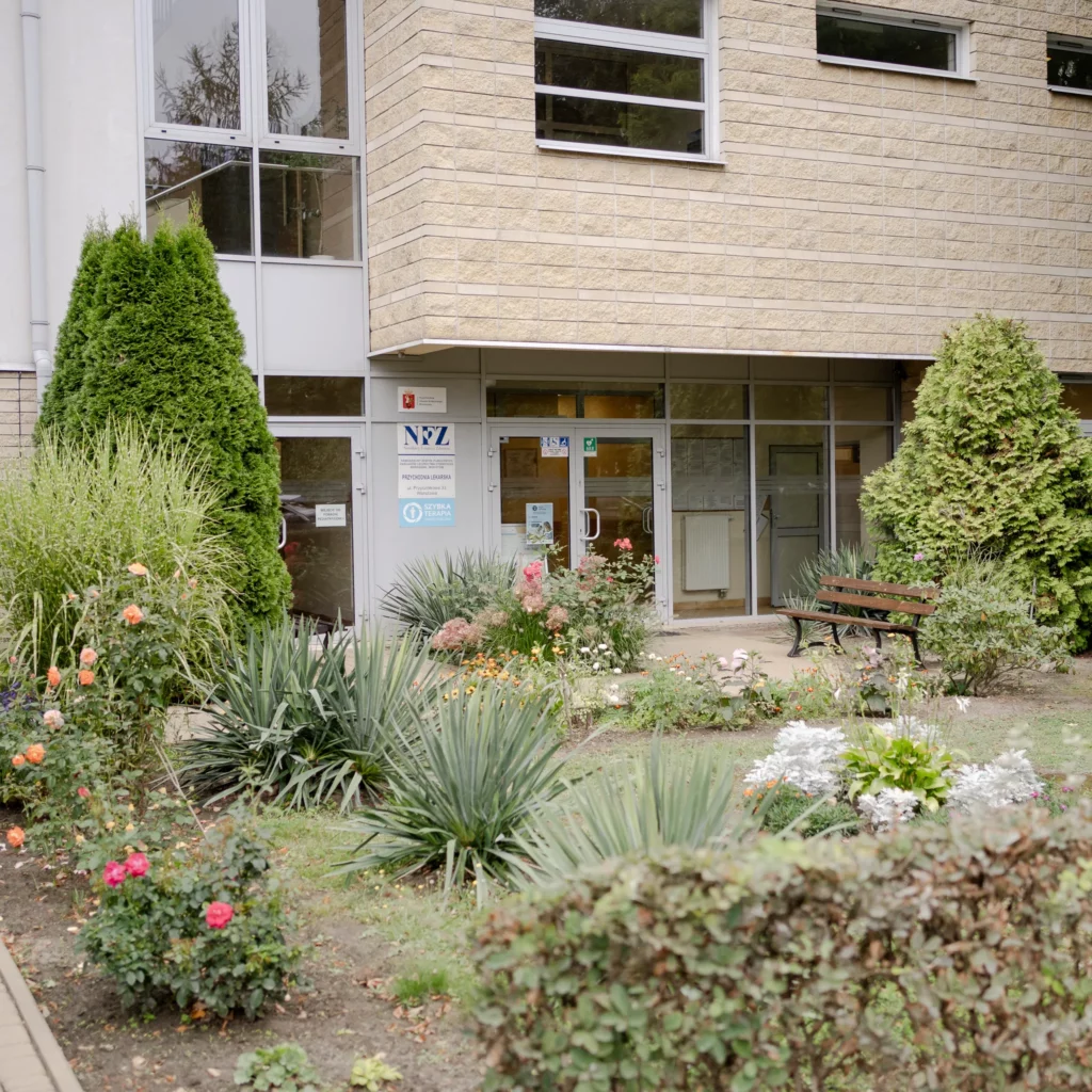Wejście do przychodni z ogrodem i ławką przed budynkiem