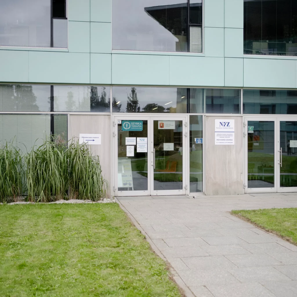 Wejście do nowoczesnego budynku przychodni lekarskiej z oznaczeniami NFZ
