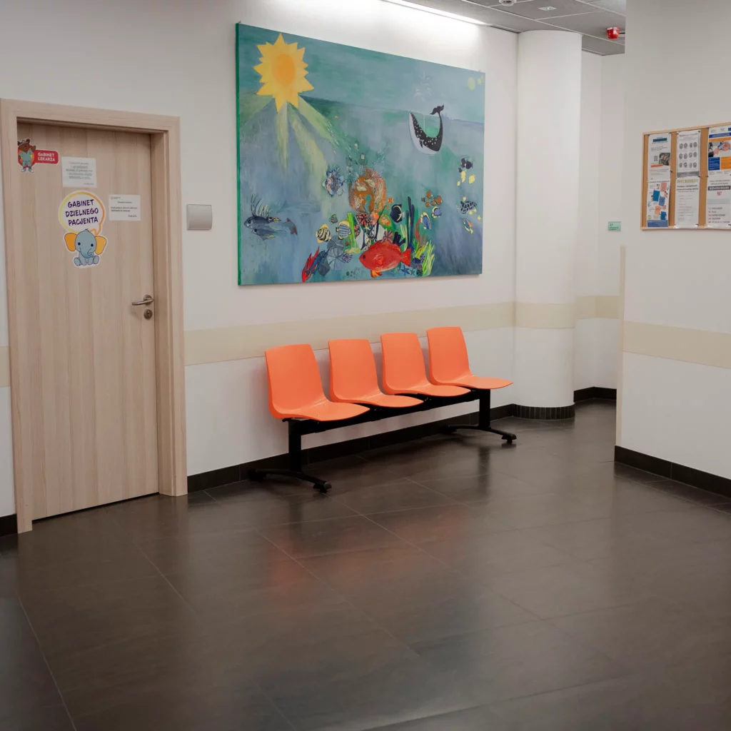Poczekalnia w przychodni z pomarańczowymi krzesłami i kolorowym obrazem na ścianie