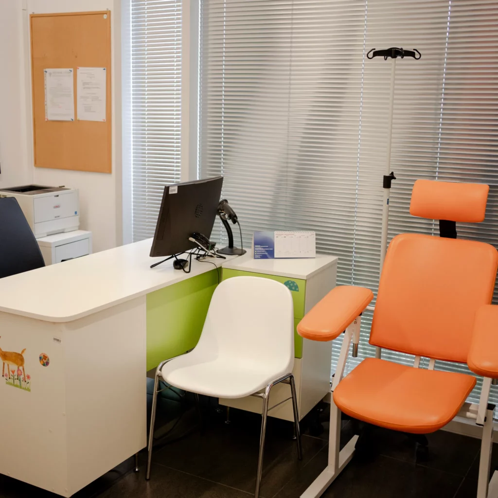 Gabinet lekarski z biurkiem, komputerem i pomarańczowym fotelem zabiegowym