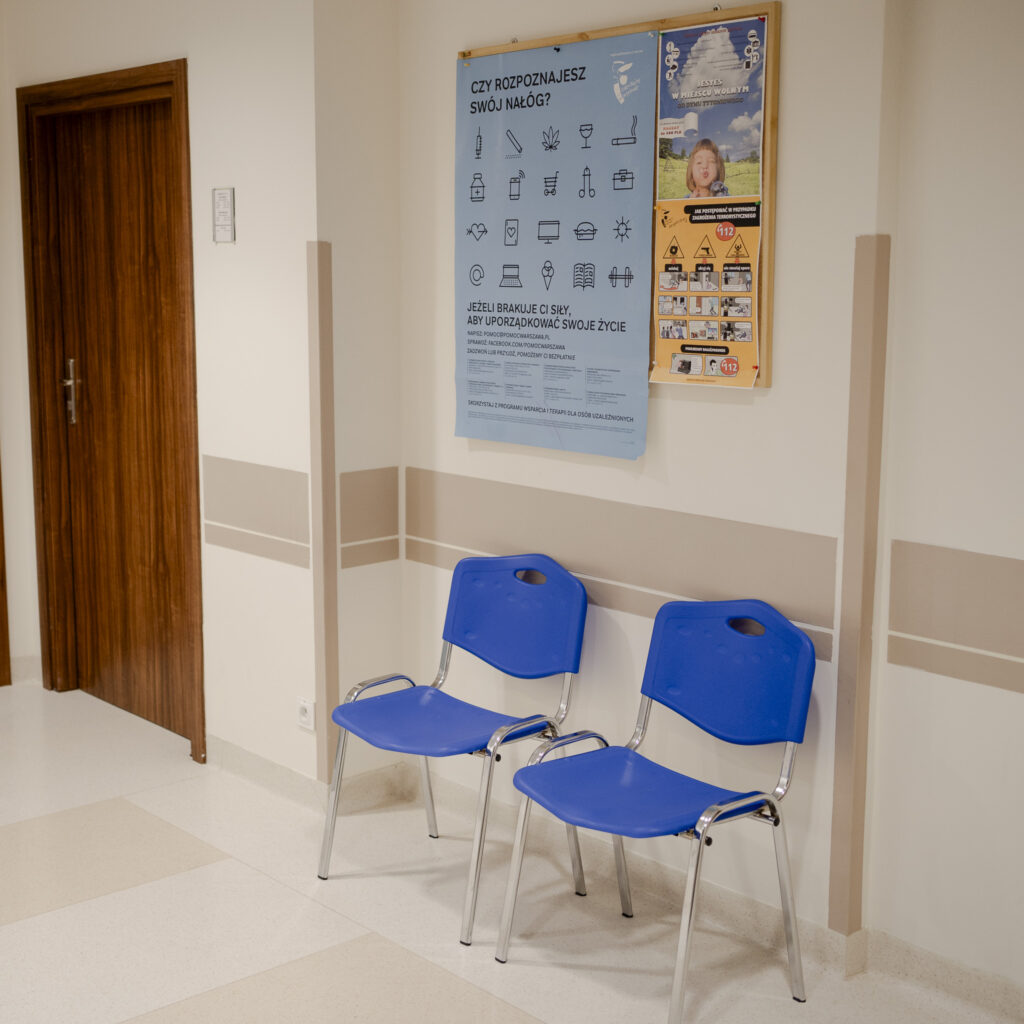 Poczekalnia w przychodni z dwoma niebieskimi krzesłami i plakatami na ścianie