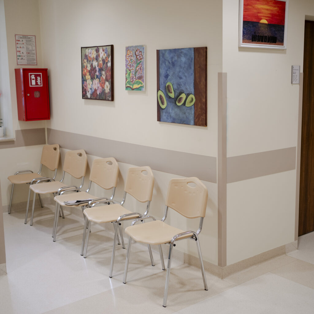 Poczekalnia w przychodni z beżowymi krzesłami i kolorowymi obrazami na ścianie