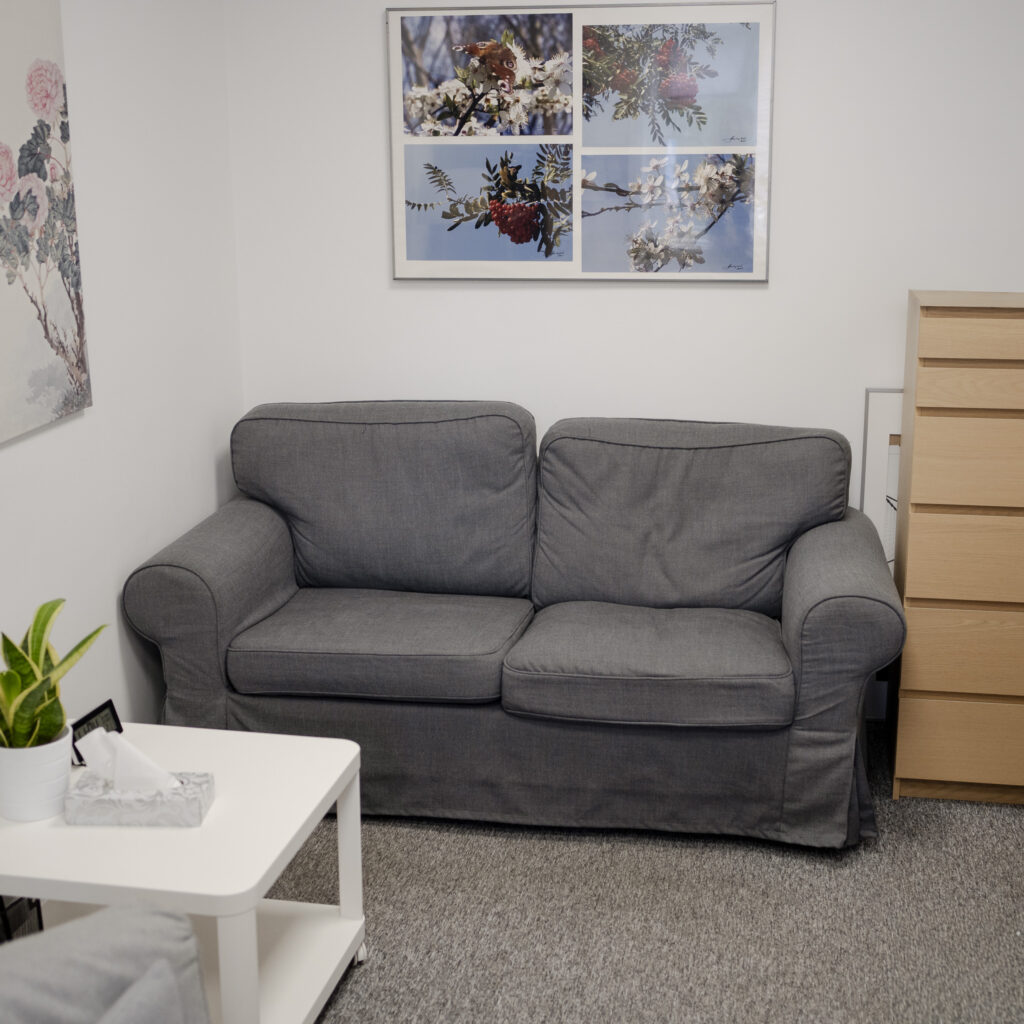Przytulny gabinet z szarą kanapą, stolikiem i rośliną doniczkową