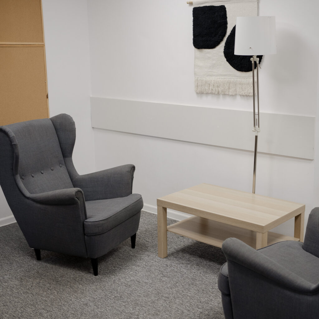 Gabinet terapeutyczny z dwoma szarymi fotelami, stolikiem i lampą stojącą