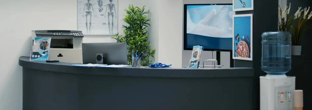 Biurko recepcyjne z monitorem komputerowym i butelkami wody.